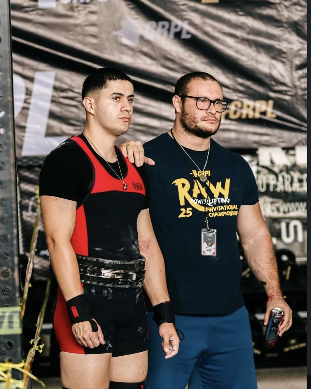 Douglas Lutz standing with one of his athletes in front of the CRPL backdrop at a competition