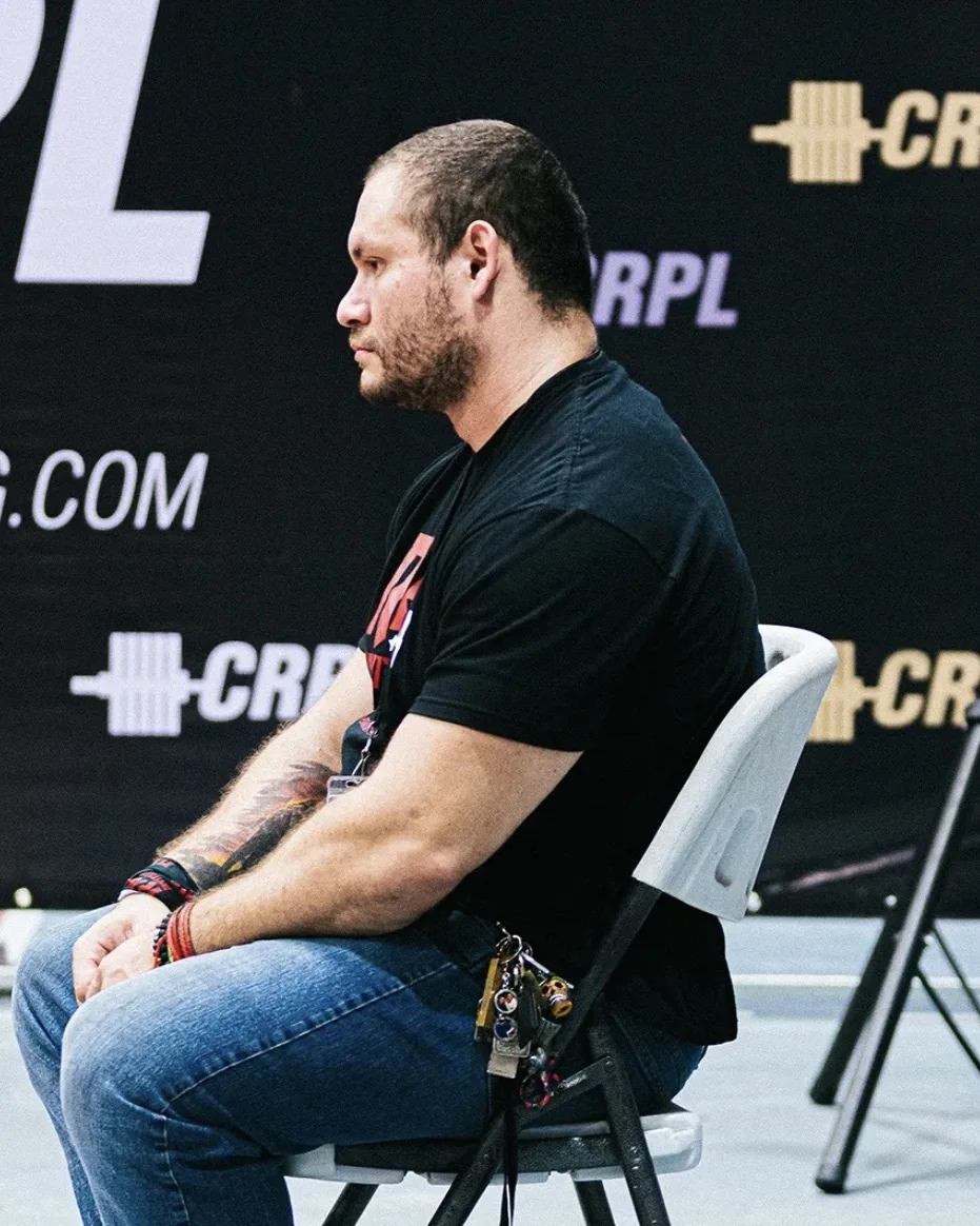 Douglas Lutz sitting beside the platform in front of the CRPL backdrop between attempts