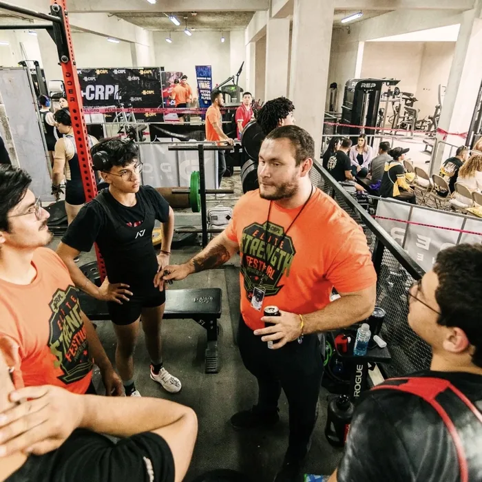 Douglas Lutz talking with athletes in Elite Strength Festival shirts before lifting